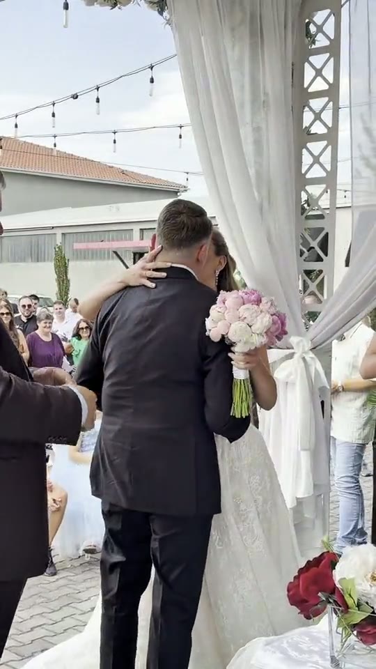 Poljubac mladenaca ispod cvetnog luka na ceremoniji venčanja na otvorenom
